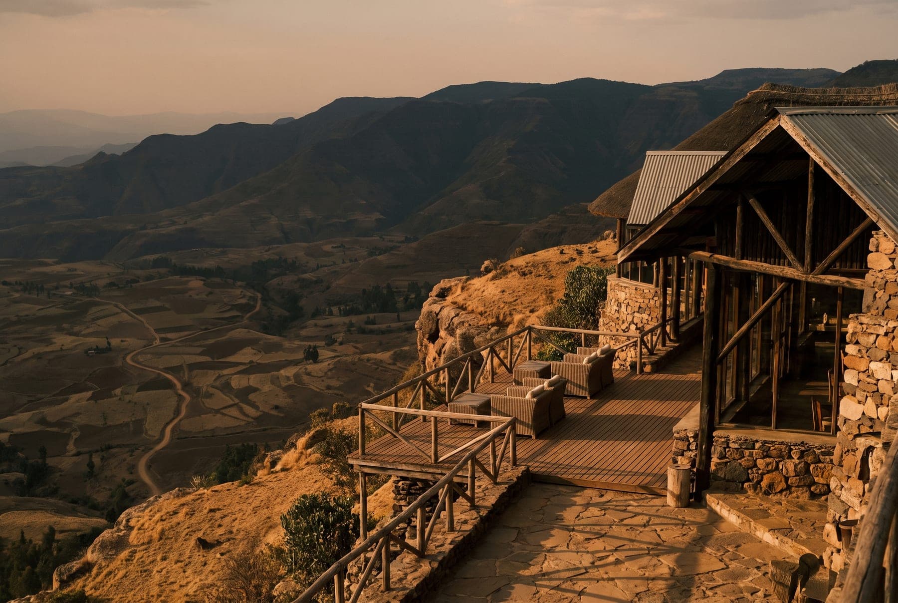 An empty terrace at a stone-and-timber highland lodge in Ethiopia overlooks a valley from an escarpment at golden hour